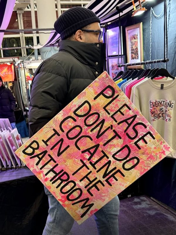 Luis carrying his Please Don't Do Cocaine in the Bathroom sign through Jubilee Market Hall